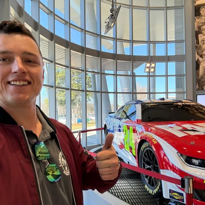 Billy giving a thumbs up next to a race car on display