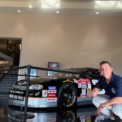 Billy next to a classic stock car in a race team lobby